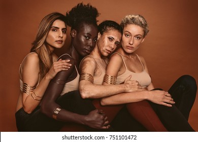 Group Of Diverse Women Sitting Together Against Brown Background. Multi Ethnic Females With Different Skin Tones In Studio.