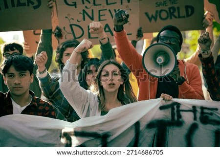 Group of diverse young activists protesting outdoors, raising fists, shouting slogans while holding banners and signs during a climate demonstration. Youth standing together for environmental change