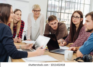 Group Of Diverse Young Adults In A Meeting With A Manageress Or University Tutor Sitting Grouped Around A Table In A Bright Spacious Office