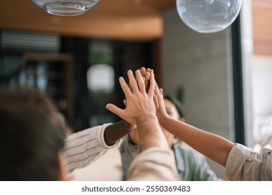 A group of diverse young business professionals in casual work attire joyfully engage in a high-five, symbolizing team success in a contemporary office environment. - Powered by Shutterstock