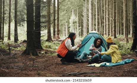 Group of diverse young female friends sitting at their forest campsite drinking coffee and reading a trail map
