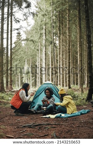 Group of diverse young female friends relaxing together at their campsite in a forest 