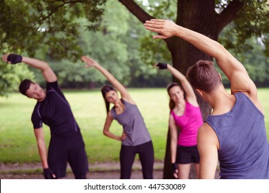 Group of diverse young friends doing outdoor aerobic exercises in a park following the lead of a male instructor - Powered by Shutterstock