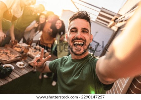 group of diverse young friends partying on rooftop eating and drinking alcohol selfie - focus on handsome guy smiling -