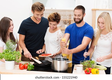 Group of diverse young friends preparing dinner together in the kitchen standing at the counter and hob cooking spaghetti and salads - Powered by Shutterstock