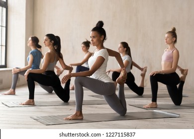 Group of diverse young sporty people doing Horse rider exercise, anjaneyasana pose, working out indoor, mixed race female students training, yoga lesson at club or studio. Well being, wellness concept - Powered by Shutterstock