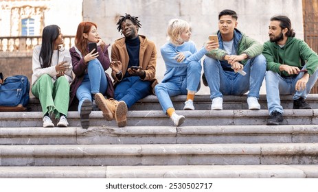 Group of diverse young students sitting on university steps, using smartphones and socializing. Multicultural friends enjoying time together on campus. Higher education, diversity, and modern student  - Powered by Shutterstock