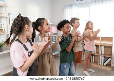 Group of diversity adorable student clapping hands at nursery school. Adorable schoolboy and girl feel happy and enjoy back to school, learning with teacher in classroom at elementary kindergarten.