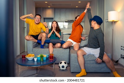 Group of diversity Asian friends sit on sofa watching and cheering soccer sports team on TV. Excited millennial people sport fans celebrate favorite football team victory in national match together