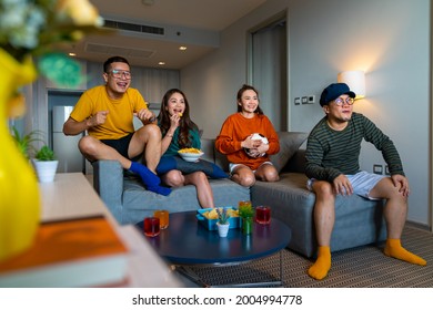 Group Of Diversity Asian Friends Sit On Sofa Watching And Cheering Soccer Sports Team On TV. Excited Millennial People Sport Fans Celebrate Favorite Football Team Victory In National Match Together