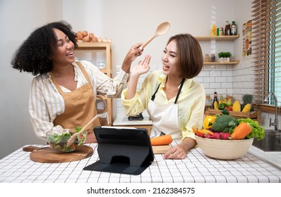 Group Of Diversity Are Cooking And Tease In The Kitchen. Group Of Friends Happily Passing Time Together And Making Salad From Vegetables In Light Modern Kitchen. Organic Food And Healthy