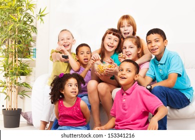Group Of Diversity Looking Kids, Boys And Girls Sitting On The Coach, Laugh, Change Channels On TV And Eat Popcorn While Watching Movie