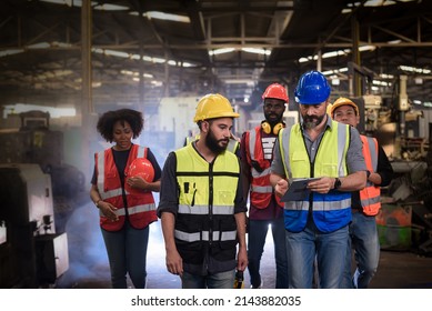 Group Of Diversity Teamwork, Engineers, Technician And Workers Team In Safety Uniform Having Discussion While Walking Through Heavy Industry Manufacturing Factory.