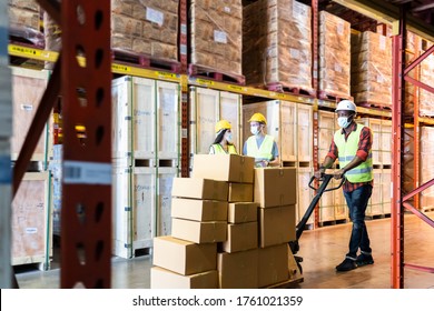 Group Of Diversity Workers Wearing Protective Face Mask Working In Factory Warehouse. Black Man Pushing Metal Lathe Cart With Box Parcel During Covid 19 Pandemic Crisis. Logistic Industry Concept.