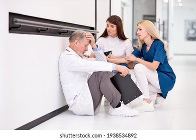 Group of doctors calm down sad colleague sitting on floor in corridor of hospital