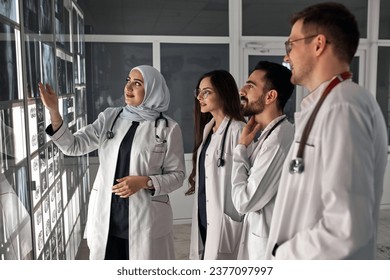 A group of doctors discusses the diagnosis of X-rays in the office. Fracture of the leg and hip joint. In the background, an Arabian professor explains to students physicians anatomy - Powered by Shutterstock