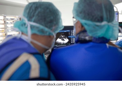 A group of doctors looking at a picture of a sonogram, TAVI Transcatheter Aortic Valve Implantation, surgery of the aortic valve, a couple of doctors in scrubs looking at a monitor
					