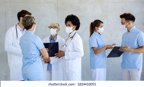 Group Of Doctors And Nurses Wearing Protective Face Masks While Communicating In A Lobby At Medical Clinic. 