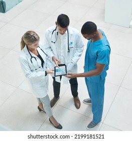 Group Of Doctors Working On Digital Tablet While Standing In The Hospital Hallway And Talking. Top View Of Healthcare Employees Analyzing Test Results And Treatment In Medicare Clinic With Technology