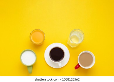 Group Of Drinks In Multicolored Cups, Black Coffee, Coffee With Milk, Yogurt, Just Water, Orange Juice On Yellow Background. Flat Lay, Top View.