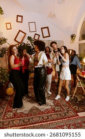 A group of eight friends are dancing while smiling and singing, three of them holding microphones, in a living room, at a party