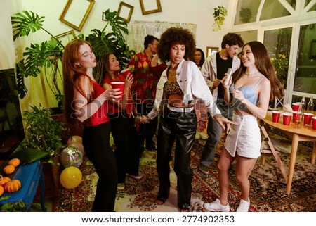 A group of eight friends are dancing while two of them are holding cups and two of them are holding microphones
