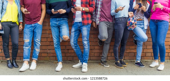 Group of eight teen friends millennials boys and girls watching smart mobile phones lean brick wall background. Concept of youth, tech, social and friendship