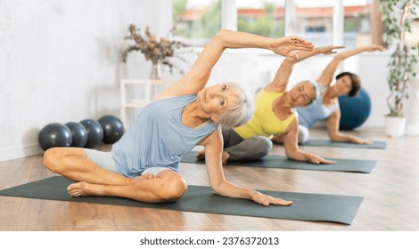 Group of elderly athletic women doing yoga on mats in fitness room - Powered by Shutterstock