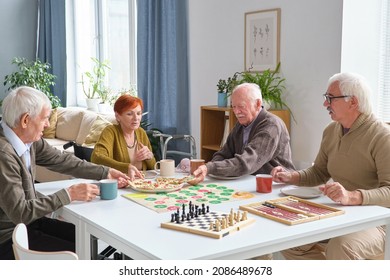 Group Of Elderly Friends Eating Pizza At The Table After Board Game In The Living Room