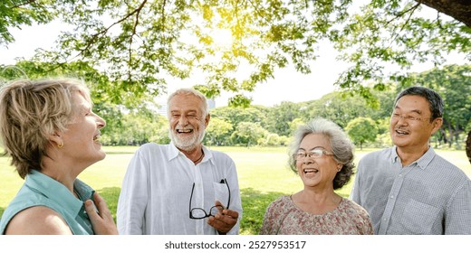 Group of elderly friends enjoy sunny day in park, smile and laugh. Elderly friends laugh and have fun outdoors, enjoy nature in park. Diverse group of elderly friends smile in nature, have fun in park - Powered by Shutterstock