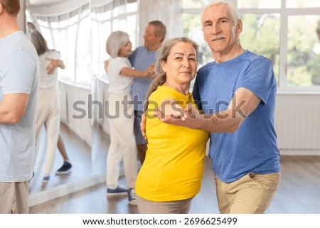 Group of elderly pensioners learn to dance a couple tango dance in a dance class