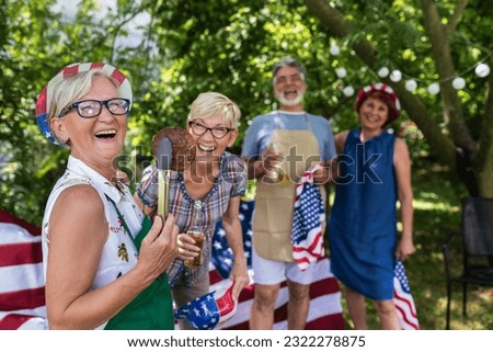 A group of elderly people celebrates the 4th of July in a backyard. They are making barbeque, vegetables, drinking beverages, making jokes, and laughing.