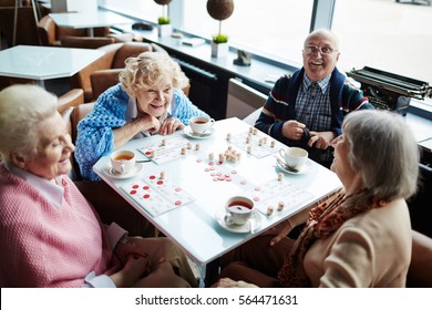 Group Of Elderly People Sitting By Table, Talking And Playing Lotto