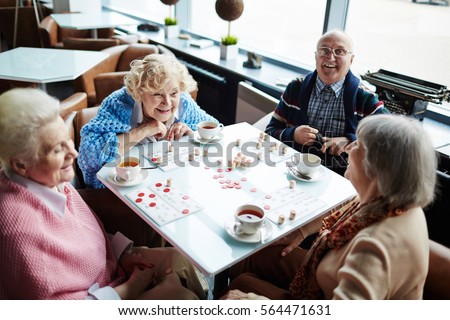 Group of elderly people sitting by table, talking and playing lotto