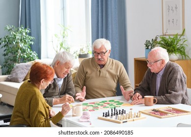 Group of elderly people sitting at the table and playing board game in the room - Powered by Shutterstock