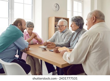 Group of elderly people are talking and having good time together sitting at table at home. Cheerful elderly people talking while sitting at table in modern retirement home. Senior social life concept - Powered by Shutterstock