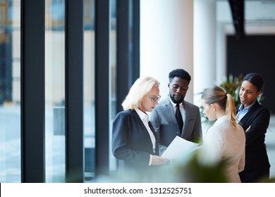 Group of elegant delegates or brokers in formalwear looking through financial papers in lounge of airport - Powered by Shutterstock