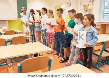 Group of elementary school children singing song during choir practice with teacher in classroom