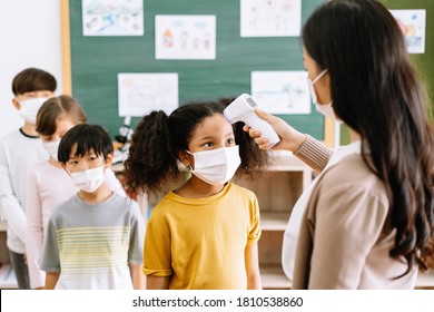 Group Of Elementary School Pupils With Face Mask Stood In Line Let The Teacher Check, Scan Thermometer Temperature For Fever Against The Spread Virus In Classroom After Covid-19 Quarantine,lockdown.