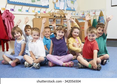 Group Of Elementary School Pupils Putting Hands Up In Class