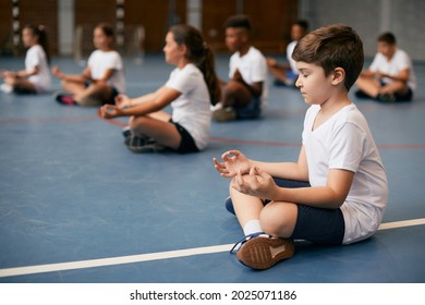 Group of elementary students doing breathing exercise while practicing yoga during physical education class at school. Focus is on a boy in foreground.  - Powered by Shutterstock