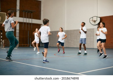 Group Of Elementary Students Having PE Class With Their Sports Teacher At School Gym.