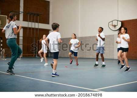 Group of elementary students having PE class with their sports teacher at school gym.