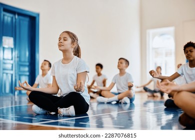 Group of elementary students practicing Yoga with eyes closed while having PE class at school gym. Focus is on girl. - Powered by Shutterstock