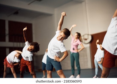 Group of elementary students warming up while doing stretching exercises on PE class at school gym. Focus is on happy boy looking at camera. 