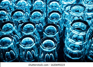 Group Of Empty Clean Glasses For Water And Cocktails Upside Down On A Table In A Row In Blue Tone. Top View In A Nightclub Under The Bar