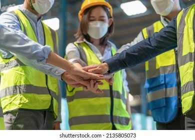 Group of Engineer and workers wear safety vests with helmets join hands to collaborate with team working in factory