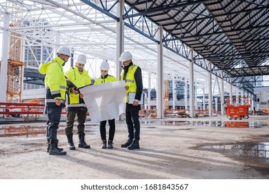 Group Of Engineers With Blueprints Standing On Construction Site.