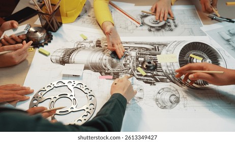 A group of engineers collaborating on technical drawings of an engine, showcasing hands interacting with tools and components, emphasizing teamwork and creativity. SACTR