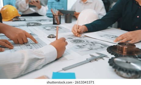 A group of engineers and professionals collaborates on mechanical designs, reviewing technical drawings and measurements in a modern workshop setting, showcasing teamwork. SACTR